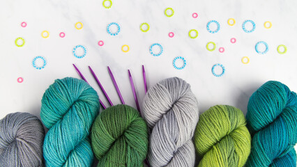 Cool yarn colors on a white background with colorful stitch markers