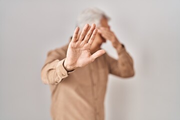 Hispanic senior man wearing glasses covering eyes with hands and doing stop gesture with sad and...