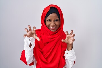 Young arab woman wearing traditional islamic hijab scarf smiling funny doing claw gesture as cat,...