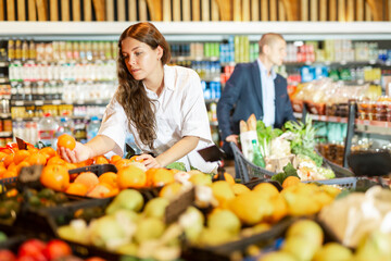 Young woman maintaining healthy lifestyle looking for fresh organic fruits and vegetables at supermarket