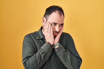 Plus size hispanic man with beard standing over yellow background tired hands covering face, depression and sadness, upset and irritated for problem