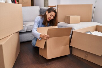 Young woman moving to a new home looking inside cardboard box smiling and laughing hard out loud because funny crazy joke.
