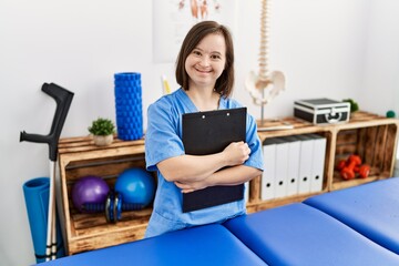 Brunette woman with down syndrome working holding clipboard at physiotherapy clinic