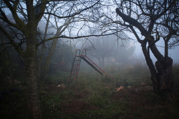 Parque infantil desolado y abandonado cubierto de niebla al anochecer  - obrazy, fototapety, plakaty