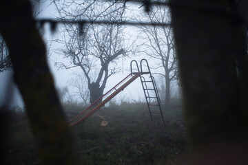 Parque infantil desolado y abandonado cubierto de niebla al anochecer - obrazy, fototapety, plakaty