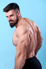 Young happy bodybuilder posing from the back, showing his back muscles and looking over his shoulders