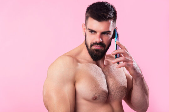 Shirtless strong bodybuilder talking on his cell, using a smartphone, pink studio background