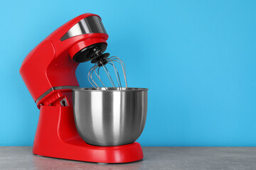 Modern red stand mixer on gray marble table against turquoise background, space for text