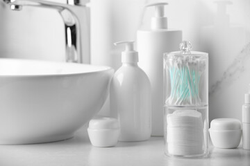 Fototapeta premium Containers with cotton swabs and pads near cosmetic products on white countertop in bathroom
