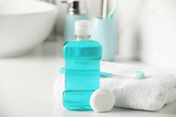 Mouthwash, toothbrush, towel and dental floss on white countertop in bathroom