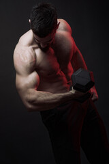 Young shirtless bodybuilder lifting a heavy dumbbell, studio image, dark background, dramatic atmosphere