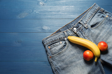 Men jeans, banana and nectarines symbolizing male genitals on blue wooden table, top view with...