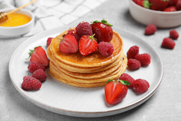 Tasty pancakes with fresh berries and honey on light grey table, closeup