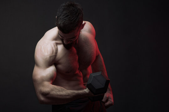 Young shirtless bodybuilder lifting a heavy dumbbell, studio image, dark background, dramatic atmosphere