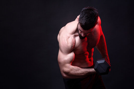Dramatic image of a strong shirtless bodybuilder lifting a heavy dumbbell, studio image, dark background, dramatic atmosphere