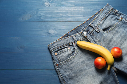 Men jeans, banana and nectarines symbolizing male genitals on blue wooden table, top view with space for text. Potency concept