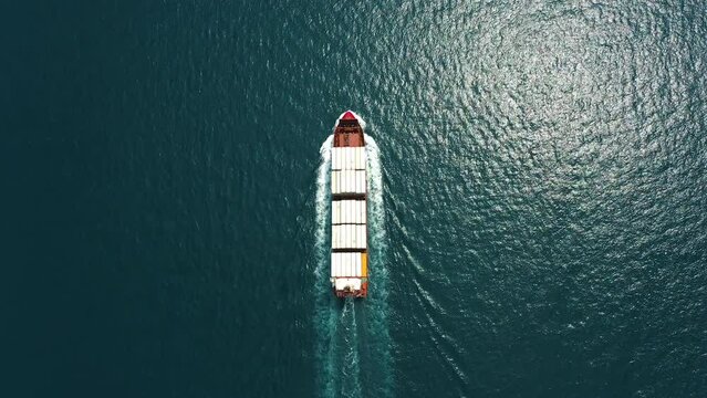 Aerial top down view: Freight ship full of containers sailing in open sea. Huge marine craft shipping import export cargo transport. Commercial business logistic