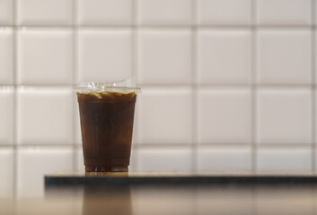 Closeup of takeaway plastic cup of iced black coffee Americano on wooden table in restaurant.