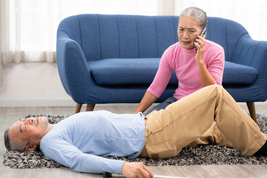An elderly man falls unconscious in the house. An elderly woman calls for an emergency. Unconscious senior man with walking stick lying on carpet at home. selective focus