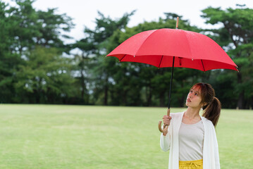 雨の公園で傘をさしている女性
