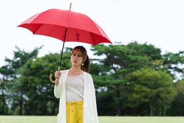 雨の公園で傘をさしている女性