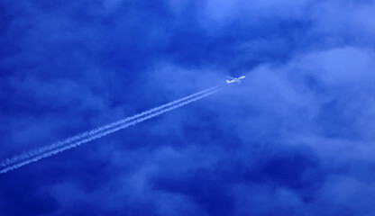 airplane in the sky with long contrails in a blue sky with some cloud cover