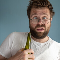 Unshaven man with tousled hair suffers from a hangover, he hugs an empty wine bottle, makes a...