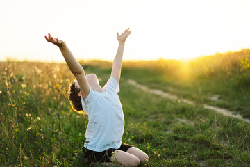 Boy closed her eyes and praying in a field at sunset. Hands folded in prayer concept for faith,...