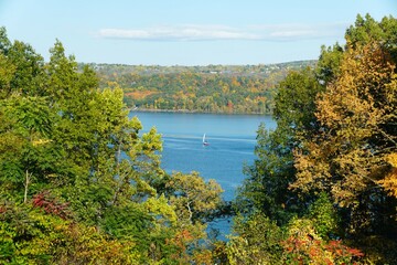 Fototapeta na wymiar A distance view of a sailboat with the background of fall foliage near Cayuga Lake, New York