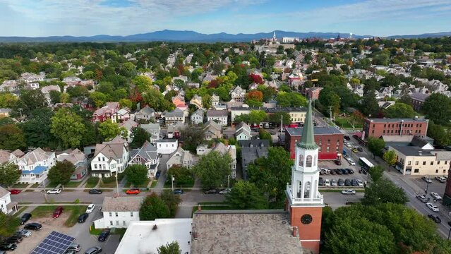 Small town America. USA city during autumn fall foliage in New England. Church steeple, colorful trees. Mountains in distance. Cinematic aerial truck shot.