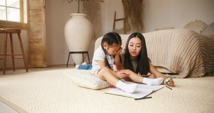 Asian mother and daughter draw color pictures in sketchbook