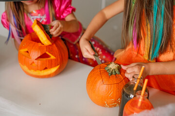 Close-up of children at the table carving pumpkin faces with a knife for the Halloween holiday. Preparation for the celebration