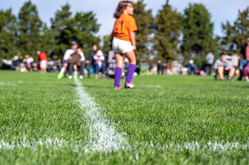 Obraz na płótnie Canvas Selective focus on ground level view of soccer field center line with defocused youth girls in background