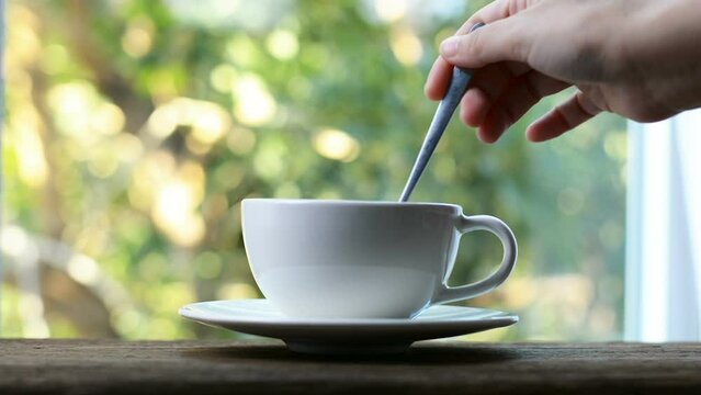 Woman's hand smoothing coffee with a spoon at the window blur tree view outside the house natural light atmosphere