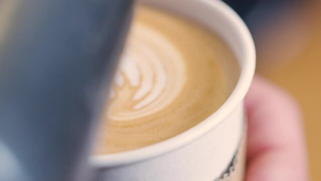 Barista pours microfoam in take away latte cup - tulip latte art; close up