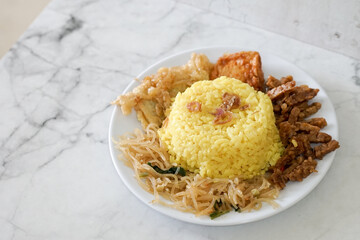 Nasi kuning, yellow rice or tumeric rice is traditional food from asia, made rice cooked with turmeric, coconut milk and spices served with egg, chicken, peanuts, chili sauce, sliced ​​cucumber, tempe