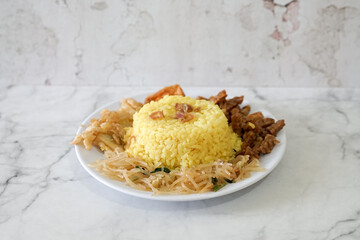 Nasi kuning, yellow rice or tumeric rice is traditional food from asia, made rice cooked with turmeric, coconut milk and spices served with egg, chicken, peanuts, chili sauce, sliced ​​cucumber, tempe