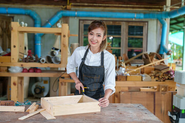 portrait of beautiful asian woman carpenter dealing with handicraft, woman has own business connected with making wooden furniture in workshop