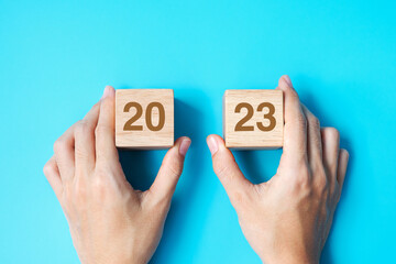 hand holding wooden cube block with 2023 text on blue background. Resolution, plan, review, goal,...