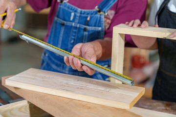 A tutor with a Female carpenter student in a workshop studying for an apprenticeship at a college using a tape measure.