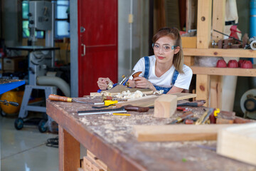 portrait of beautiful asian woman carpenter dealing with handicraft, woman has own business connected with making wooden furniture in workshop.