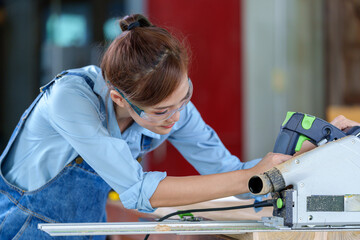 Female Carpentry Student In Workshop Studying For Apprenticeship At College Using Bench Saw