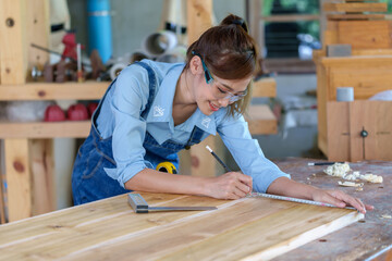 portrait of beautiful asian woman carpenter dealing with handicraft, woman has own business connected with making wooden furniture in workshop