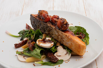Portion of salmon with cherry tomato on top and vegetables
