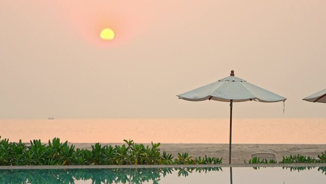 A pink and yellow sun setting over a beach umbrella. Title space