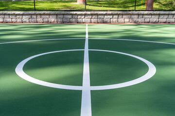 Interesting green and red outdoor basketball court at school playground.  Court includes retaining walls and black vinyl coated chain link fence.	 - Powered by Adobe