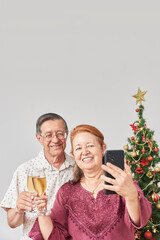 Happy senior latin couple making a selfie with a smartphone while toasting during Christmas or New Year, celebrating holidays at home, having a good time together and sharing it with their loved ones.