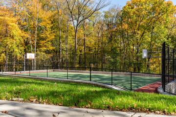 Interesting green and red outdoor basketball court at school playground.  Court includes retaining walls and black vinyl coated chain link fence.	
