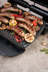 Grilled sausages and vegetables on electric grill at domestic kitchen