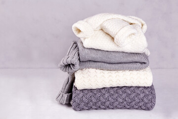 Fototapeta na wymiar Gray and white knitted sweaters stacked on a gray background. Pile of wool winter and autumn clothes. Copy space